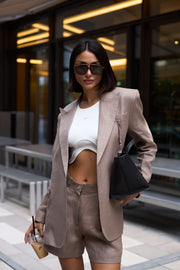 Woman in a beige suit and sunglasses standing outdoors.